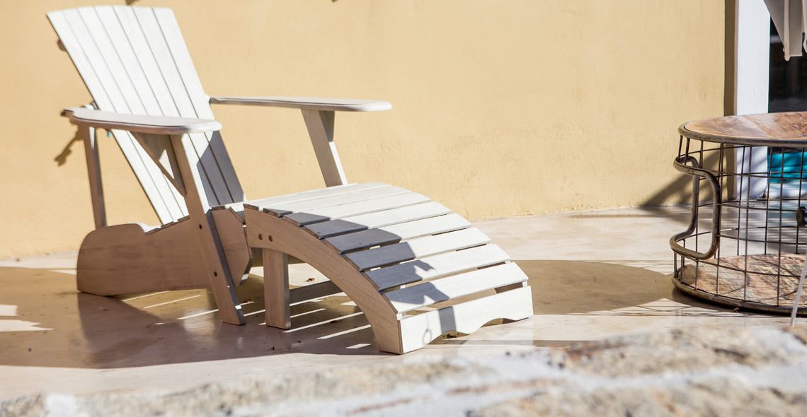 A wooden Adirondack chair with a curved backrest and armrests, positioned on a stone patio.