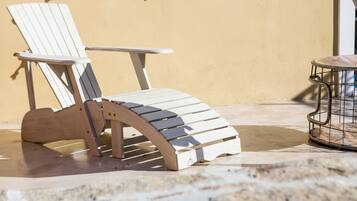 A wooden Adirondack chair with a curved backrest and armrests, positioned on a stone patio.