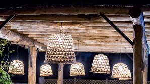 An outdoor dining area with wooden tables and chairs, and hanging lamps with a geometric pattern.