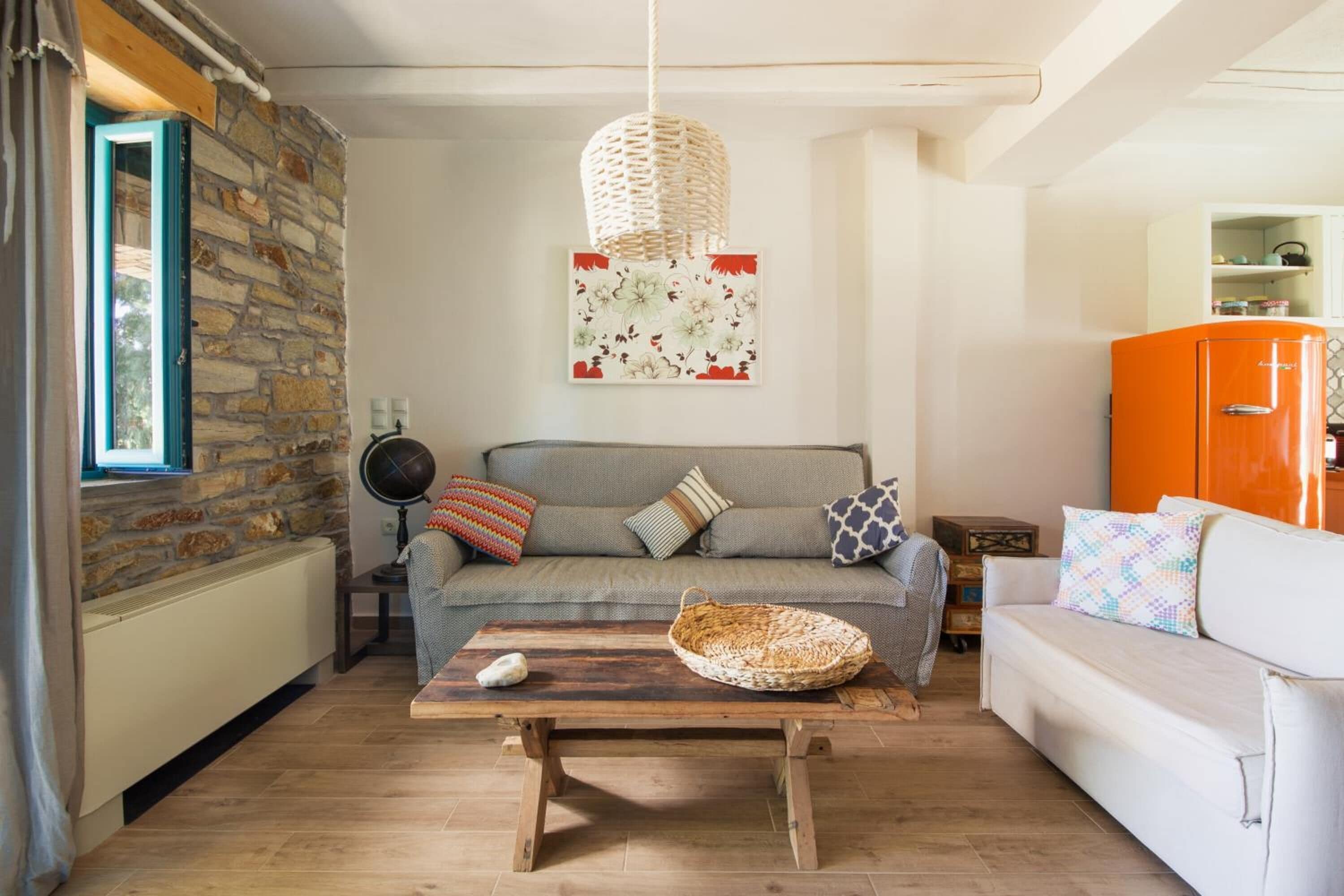 A cozy living room with a stone wall, a wooden coffee table, a sofa, and a vintage orange refrigerator.