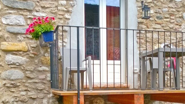A stone building with a balcony, a window, and a small outdoor seating area.
