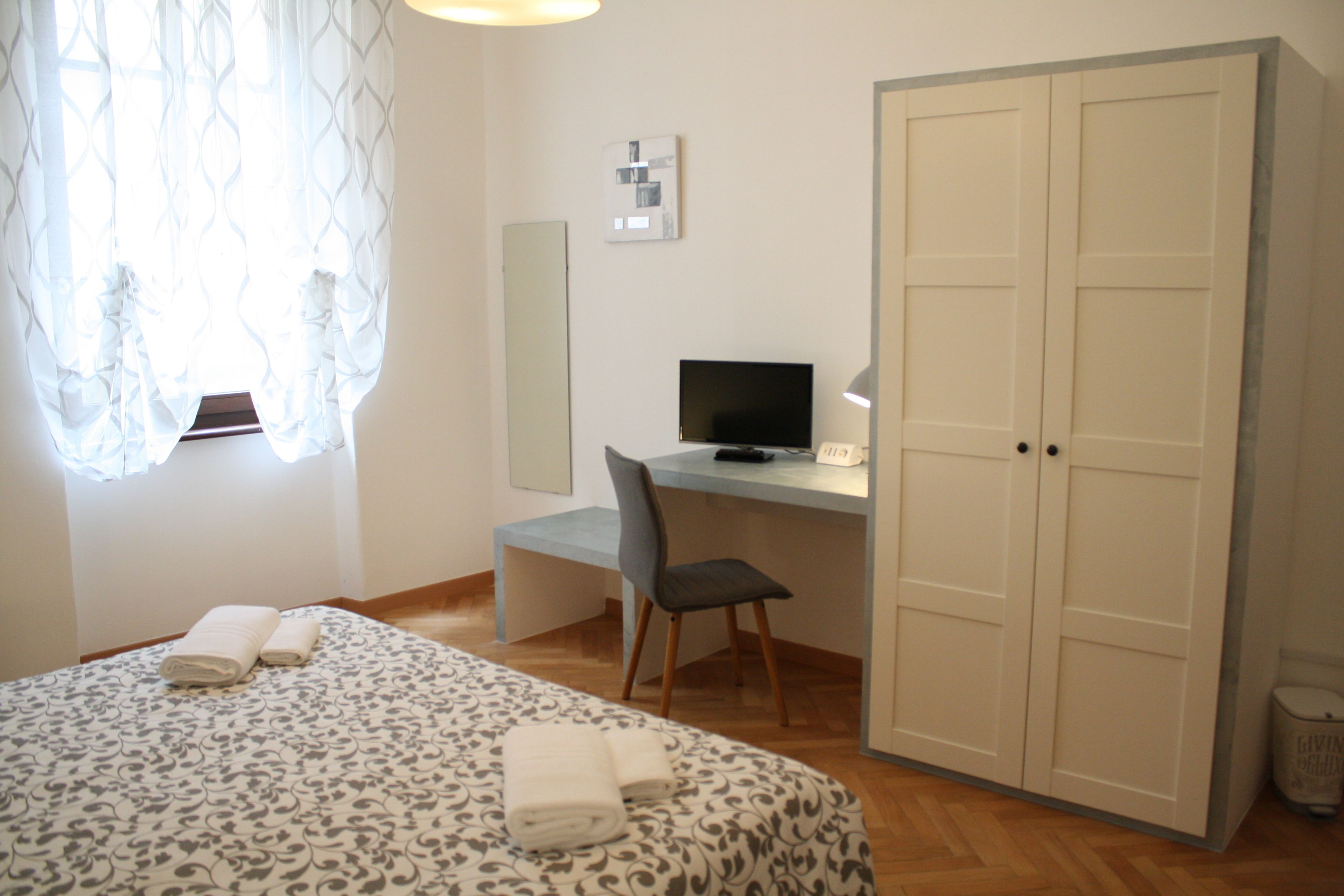 A bedroom with a bed, a desk, a chair, a television, and a wardrobe.