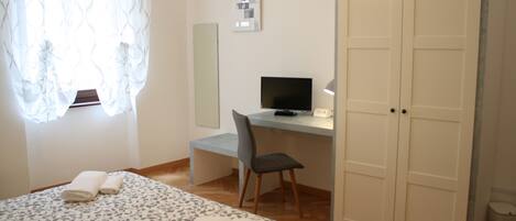 Un dormitorio con una cama, un escritorio, una silla, un televisor y un guardarropa.