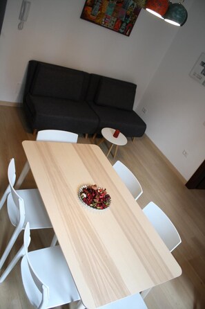 A dining area with a wooden table, white chairs, a black sofa, and a small round table.