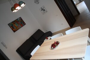 A modern dining area with a wooden table, white chairs, a black sofa, and a decorative plate of flowers.