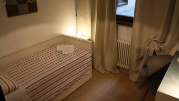 Une petite chambre avec un lit simple, une couvre-lit à motifs, un radiateur et une fenêtre avec des rideaux.