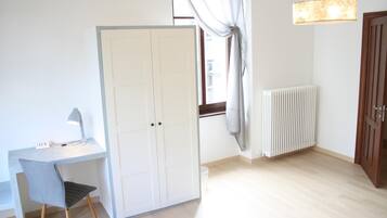 A room with a desk, chair, wardrobe, radiator, and a hanging light fixture.
