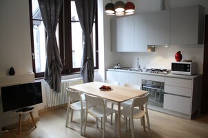A modern kitchen with white cabinets, a wooden dining table, and a TV.