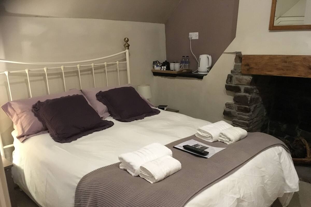 A neatly made bed with white and purple bedding, a remote control, and folded towels on a textured bedspread.