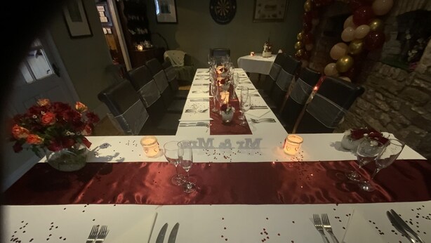 A dining table set for a meal with candles, a vase of flowers, and a decorative banner. - The Tanners Arms (Brecon)