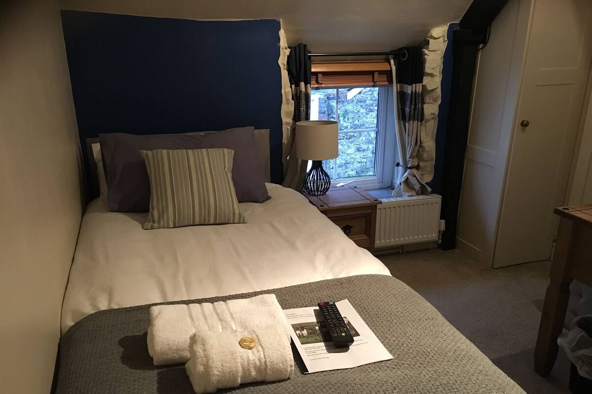A neatly made bed with pillows, a bedside table with a lamp, and a window with curtains.