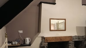 A bedroom with a stone fireplace, a bed with pillows, a bedside table with a kettle, and a mirror on the wall. - The Tanners Arms (Brecon)