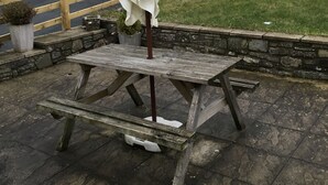 A picnic table with a white umbrella, set against a stone wall and wooden fence. - The Tanners Arms (Brecon)