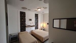 A bedroom with two beds, a bedside table with a lamp, a small desk with a phone, and a mirror on the wall. - Le Bon Geours (Saint-Geours-de-Maremne)