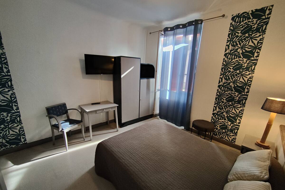 Een hotelkamer met een bed, een bureau, een stoel, een televisie en gordijnen.
