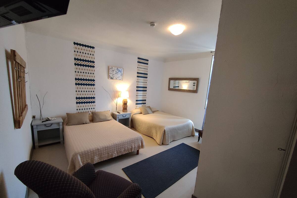 Een hotelkamer met twee bedden, een stoel, een nachtkastje met een lamp en een wandklok.