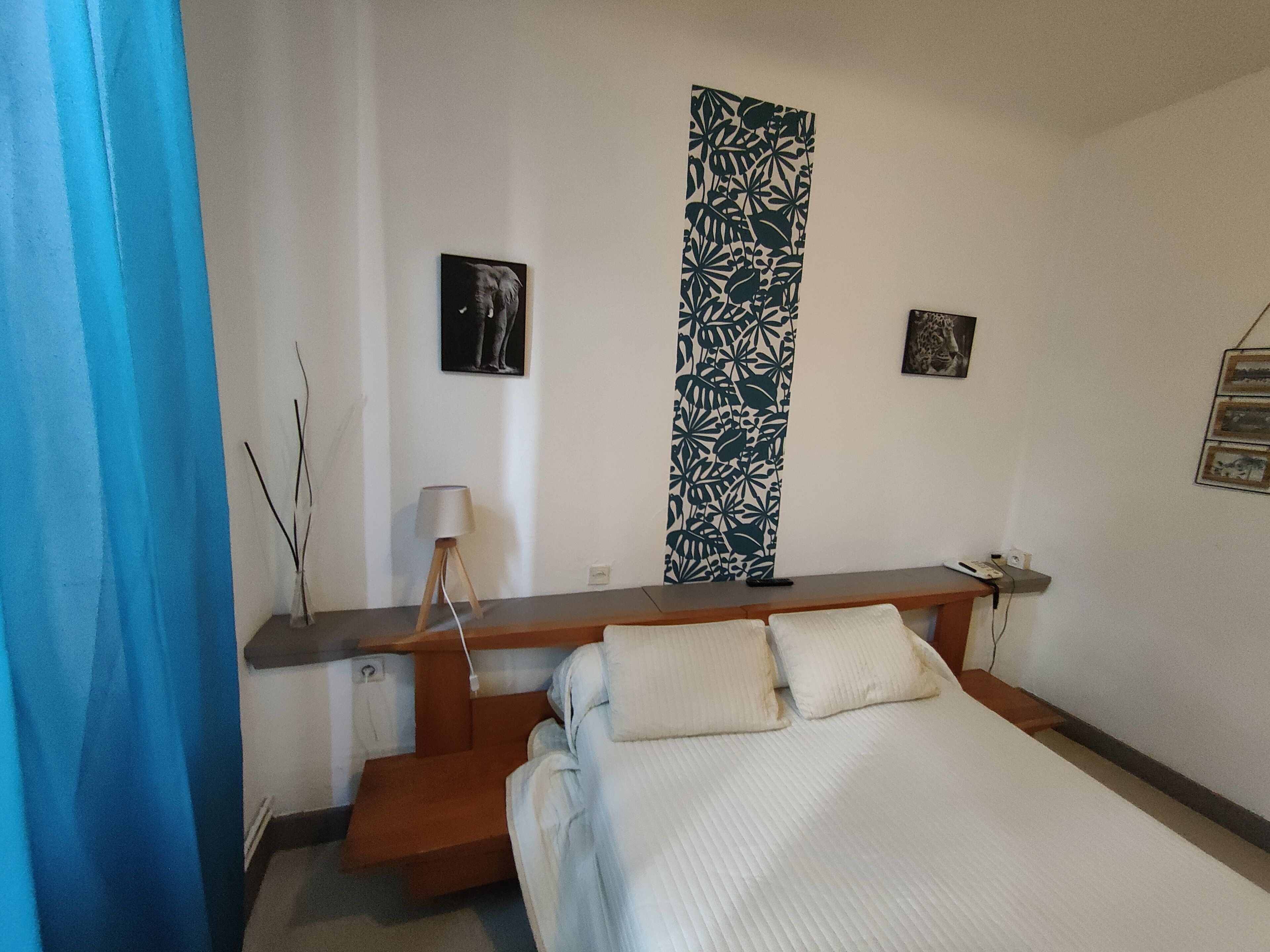 Une chambre à coucher avec un lit, une table de chevet, une lampe et un mur orné de deux tableaux encadrés.