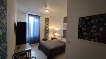 A hotel room with a bed, a desk, a chair, a nightstand, and a wall with a floral pattern.