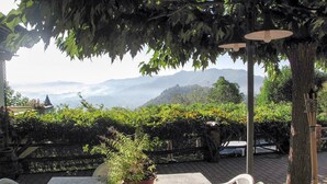 Eine Terrasse im Freien mit Tisch und Stühlen, umgeben von Grün und Blick auf ferne Berge.