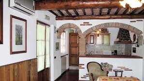 Ein rustikales Interieur mit einer hölzernen Bank, einem Tisch mit gemustertem Tischläufer und einer Küchenzeile mit gefliestem Rücksprung und Holzschränken.