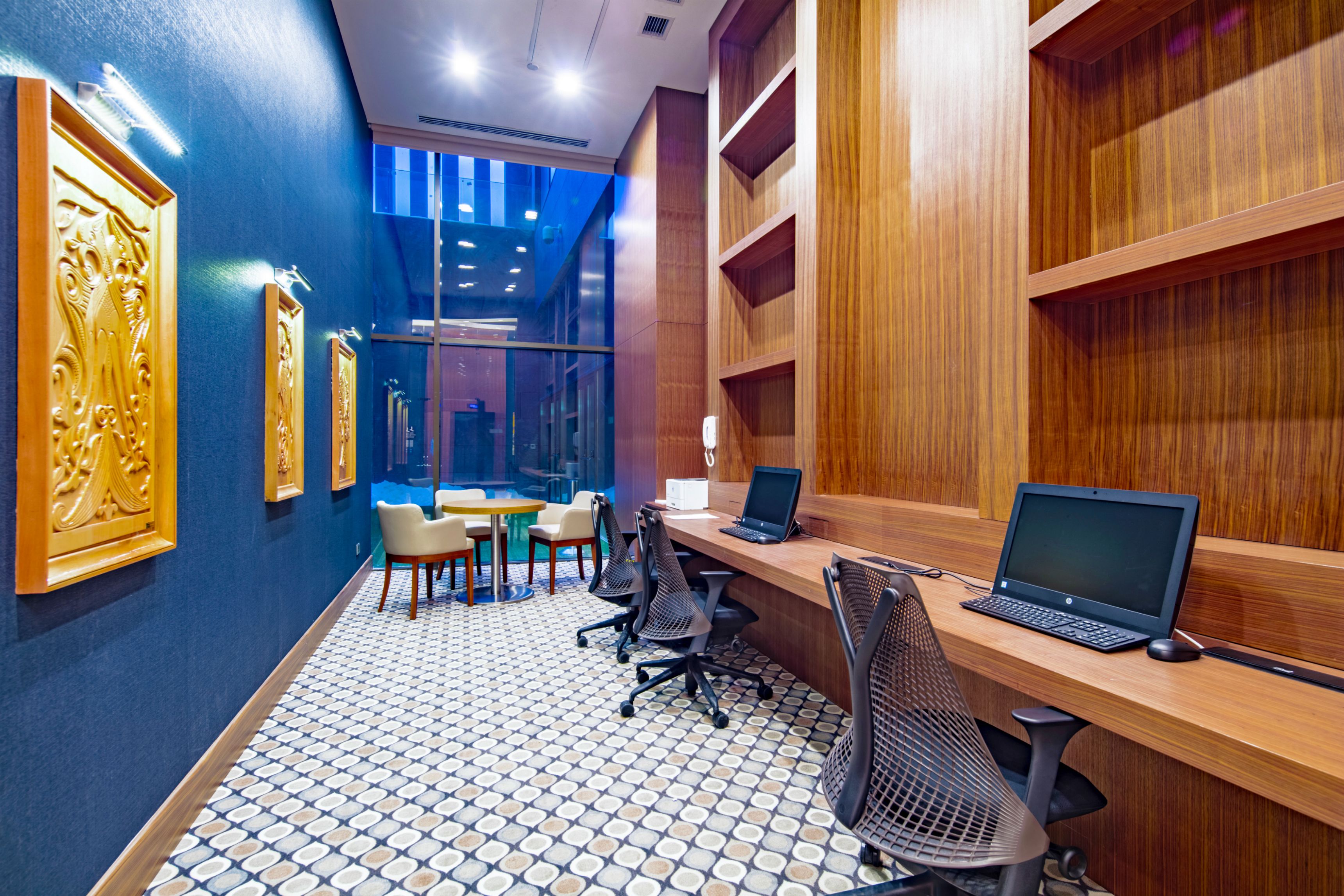 A modern office space with a long reception desk, two laptops, and a meeting table with chairs.