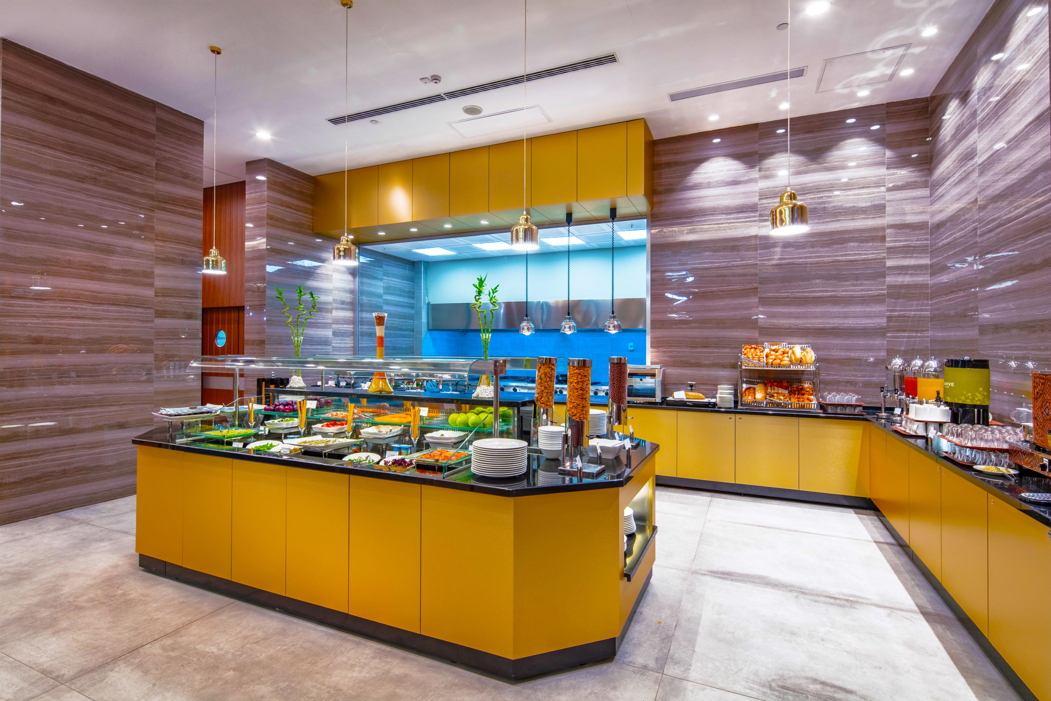 Un espace buffet doté d’un îlot central, de plusieurs luminaires suspendus et d’un design moderne aux tons jaunes et bruns.
