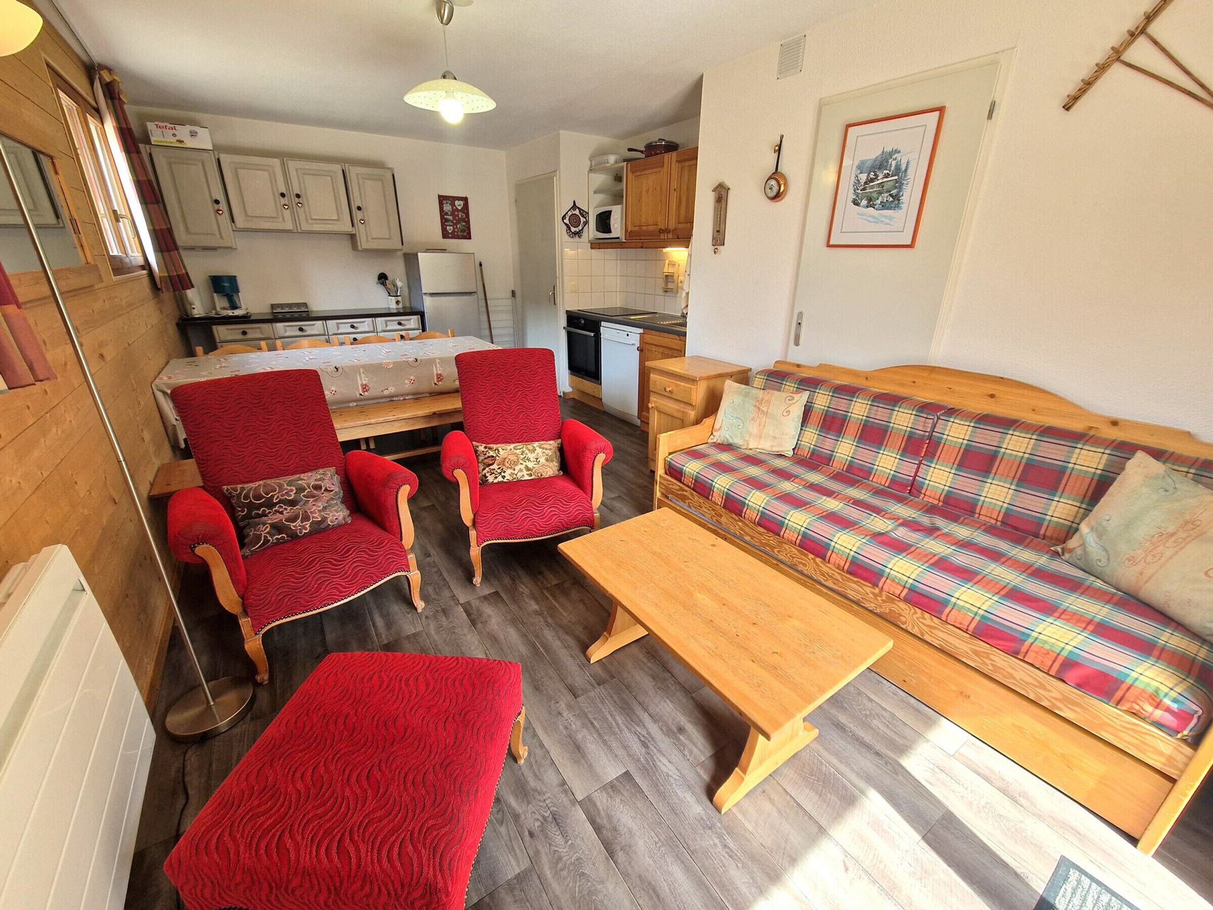 A cozy living room with a wooden sofa, two red armchairs, and a wooden coffee table.