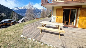 A wooden deck with a picnic table, a balcony with wooden railings, and a mountain view in the background.