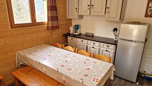 A cozy kitchen with wooden cabinets, a refrigerator, a coffee maker, and a table set with a floral tablecloth.
