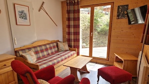 A cozy room with a wooden sofa, a red armchair, a small table, and a sliding glass door leading to an outdoor area.