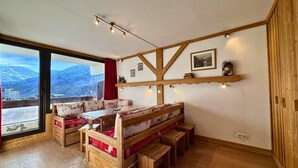 Um quarto acolhedor com um banco de madeira e uma mesa, janelas amplas com vista para as montanhas e um lustre no teto.