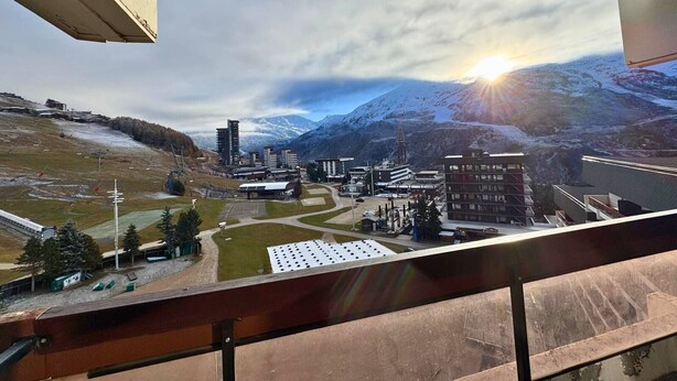Vista de uma cidade com edifícios modernos, uma pista de esqui e montanhas cobertas de neve ao fundo.