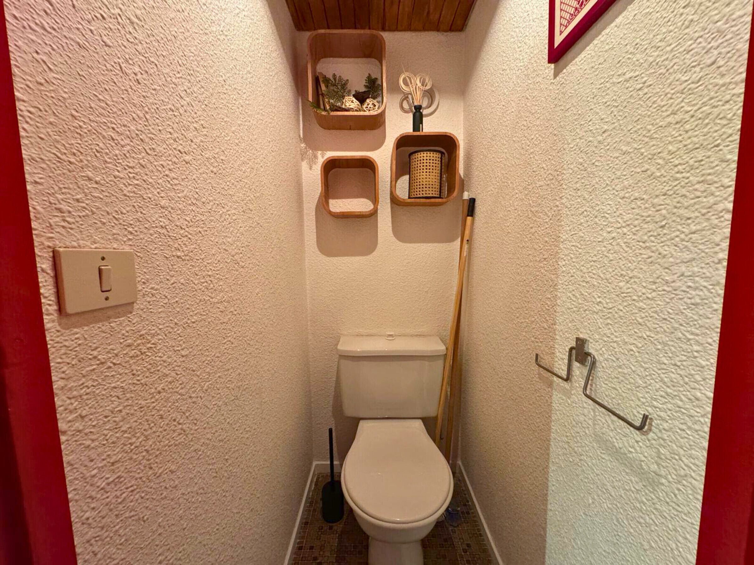 A compact bathroom with a toilet, a bidet, and a small shelf with decorative items.