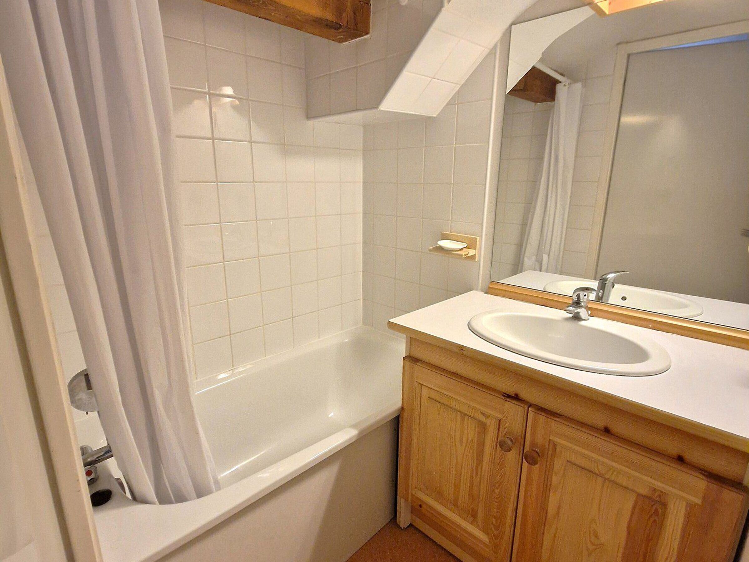 Een badkamer met een wit bad, een houten wastafelmeubel met een wastafel en een spiegel erboven.