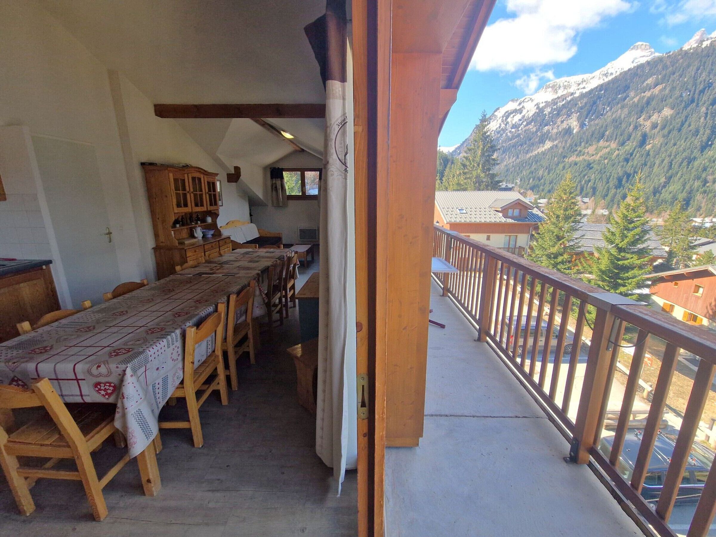 A balcony with a wooden table and chairs, a view of a mountain, and a building in the background.