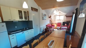 Eine kleine Küche mit weißen Schränken, einem Einbauofen und einem Essbereich mit Holztisch und Stühlen.