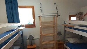 Ein Schlafraum mit Etagenbetten, einer Holzleiter, einem Fenster mit blauen Vorhängen und einem kleinen Tisch mit einer Lampe.