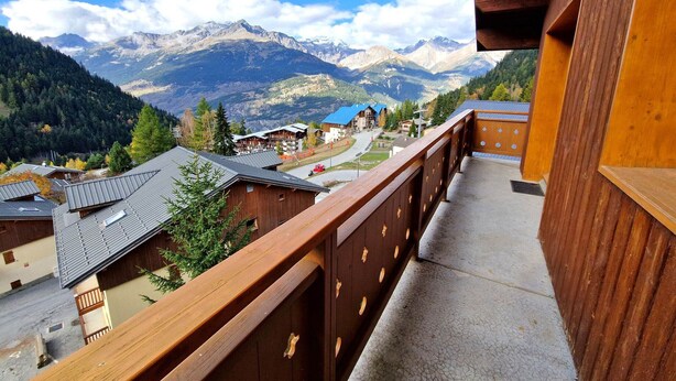 Un balcón de madera con vistas a una cadena montañosa y un pueblo pequeño al pie.