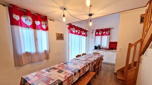 Un comedor con una mesa larga cubierta por un mantel de retazos, bancos de madera y cortinas rojas con diseños de corazones.