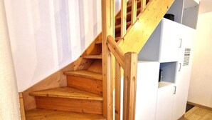 Una escalera de madera con barandilla que conduce a un módulo de almacenamiento blanco con un ventanal pequeño.
