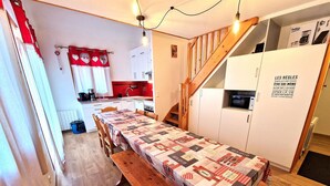 Una cocina compacta con una mesa de madera, una cortina roja y blanca, y una escalera que sube a una zona de entrepiso.