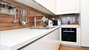 A modern kitchen with white cabinetry, a stainless steel sink, and a built-in oven. - Apartman Trnje (Zagreb)