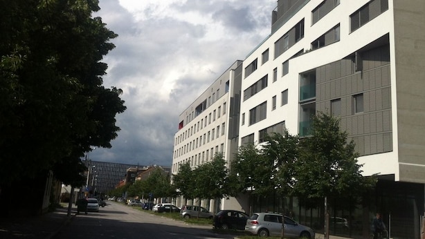 A modern building with a flat facade, multiple windows, and a parking area with cars. - Apartman Trnje (Zagreb)