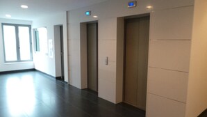 A hallway with three elevators, a door on the left, and a window on the left side. - Apartman Trnje (Zagreb)
