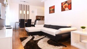 A modern living room with a sectional sofa, a dining area with a table and chairs, and a kitchen in the background. - Apartman Trnje (Zagreb)