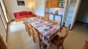 Una cocina compacta con microondas, pileta y alacenas. Hay una mesa de comedor con sillas y un sofá rojo en la zona de estar.