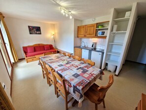 Una cocina compacta con microondas, pileta y alacenas. Hay una mesa de comedor con sillas y un sofá rojo en la zona de estar.
