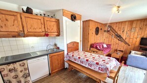 Ein gemütlicher Raum mit Holzwänden, einem Bett mit gemustertem Überwurf, einem kleinen Tisch, einem Stuhl, einem Waschbecken und einem Fernseher.