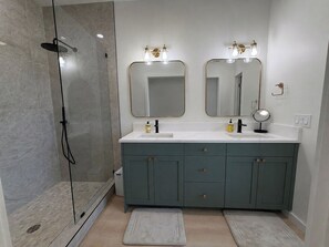 A bathroom with a shower, two sinks, and a vanity with cabinets. - Brand-new Maui home with comfort and local charm! (Lahaina)