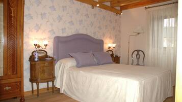 A bedroom with a large bed, wooden headboard, two bedside tables with lamps, floral wallpaper, and a wooden wardrobe.